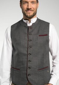 Grau Weste aus strukturiertem Stoff, Stehkragen, sieben schwarze Knöpfe, kastanienbraune Akzente an den Taschen und der Knopfleiste. Weißes Hemd darunter.
