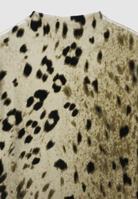 Tessuto strutturato con sfondo beige, caratterizzato da grandi macchie nere e marrone scuro, simili a stampe animali.