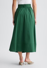 Gonna verde lungo fino alla caviglia, realizzata in tessuto leggero. Presenta una cintura elastica e una silhouette fluida con un sottile dettaglio di cucitura orizzontale.