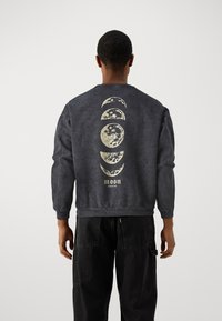 Felpa girocollo grigio scuro con una grafica delle fasi lunari in crema sul retro, con polsi e orlo a costine, realizzata in un tessuto ricco di cotone.