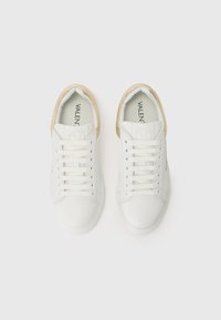 Hvite sneakers med en glatt lærtekstur, med en beige hælakkent, runde snørebånd og en logo på tungen.