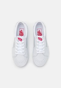 Baskets en cuir blanc avec orteil perforé, lacets et logo Vans rouge sur la languette et le côté. Design classique à tige basse. Texture lisse.