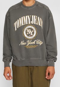 Felpa grigia con polsini e orlo a coste, caratterizzata da un grande logo giallo e bianco "TOMMY JEANS" e una stampa "New York City".