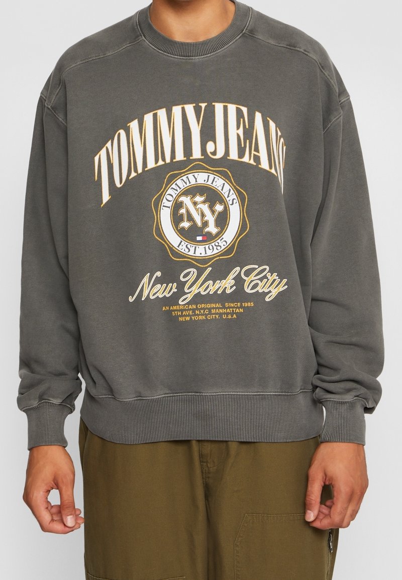 Felpa grigia con polsini e orlo a coste, caratterizzata da un grande logo giallo e bianco "TOMMY JEANS" e una stampa "New York City".