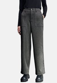 Grijze wijde broek van een gestructureerde stof, met twee voorkeurszakken en een knoopsluiting, gecombineerd met zwarte dikke laarzen.