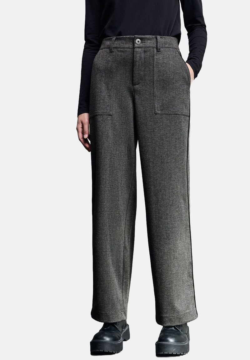 Grijze wijde broek van een gestructureerde stof, met twee voorkeurszakken en een knoopsluiting, gecombineerd met zwarte dikke laarzen.