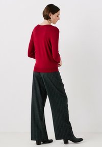 Röd tröja med långa ärmar, rund halsringning, ribbat avslut; parat med mörka rutiga vida byxor och svarta klackstövlar.