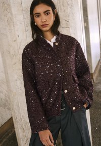 Giacca bordeaux con paillettes e finitura testurizzata, dotata di scollo rotondo, due tasche e chiusura con bottoni.