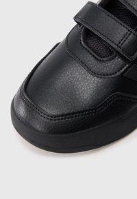 Μ�αύρο δερμάτινο αθλητικό παπούτσι με υφή στη μύτη, ιμαντάκι με βέλκρο και παχιά λαστιχένια σόλα πάνω σε λευκό φόντο.