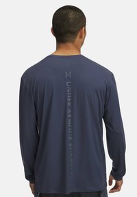 Marineblaue Langarm-Laufshirt aus feuchtigkeitsableitendem Material mit einem vertikalen Logo-Design auf dem Rücken. Glatter Stoff und lockere Passform.