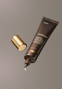 Deep Vita A Retinol Serum i en brun tube med gyldne detaljer og skruehætte. En dråbe grøn serum er synlig for enden af tuben.