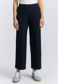 Pantaloni a gamba larga blu navy in un tessuto morbido, con pieghe frontali e vita alta, abbinati a sneakers blu chiaro.
