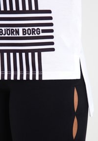 Hvid t-shirt med sorte vandrette striber og teksten "BJÖRN BORG"; sat sammen med sorte leggings, der fremhæver udskæringer.
