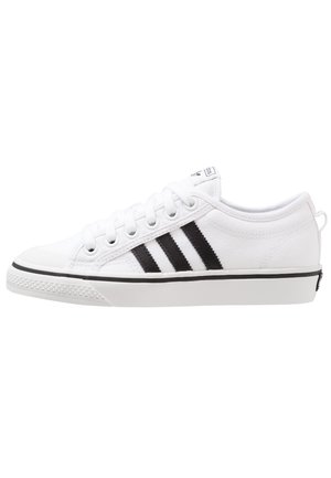 Sneaker bassa bianca con tre strisce nere sul lato, lacci bianchi e suola in gomma con bordo nero.