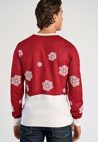 Czerwony sweter z białymi wzorami śnieżynkami. Żebrowany biały dekolt i mankiety. Dolna część swetra ma jednolitą białą sekcję. Strukturę splotu wykonano na maszynie.