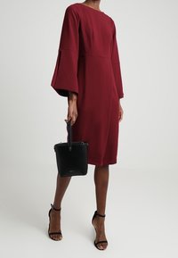 Viininpunainen mekko, jossa pitkät kellohihat, polvipituinen. Yhdistetty mustaan käsilaukkuun ja remmikkäisiin korkokenkiin. Sileä kangas, minimalistinen muotoilu.