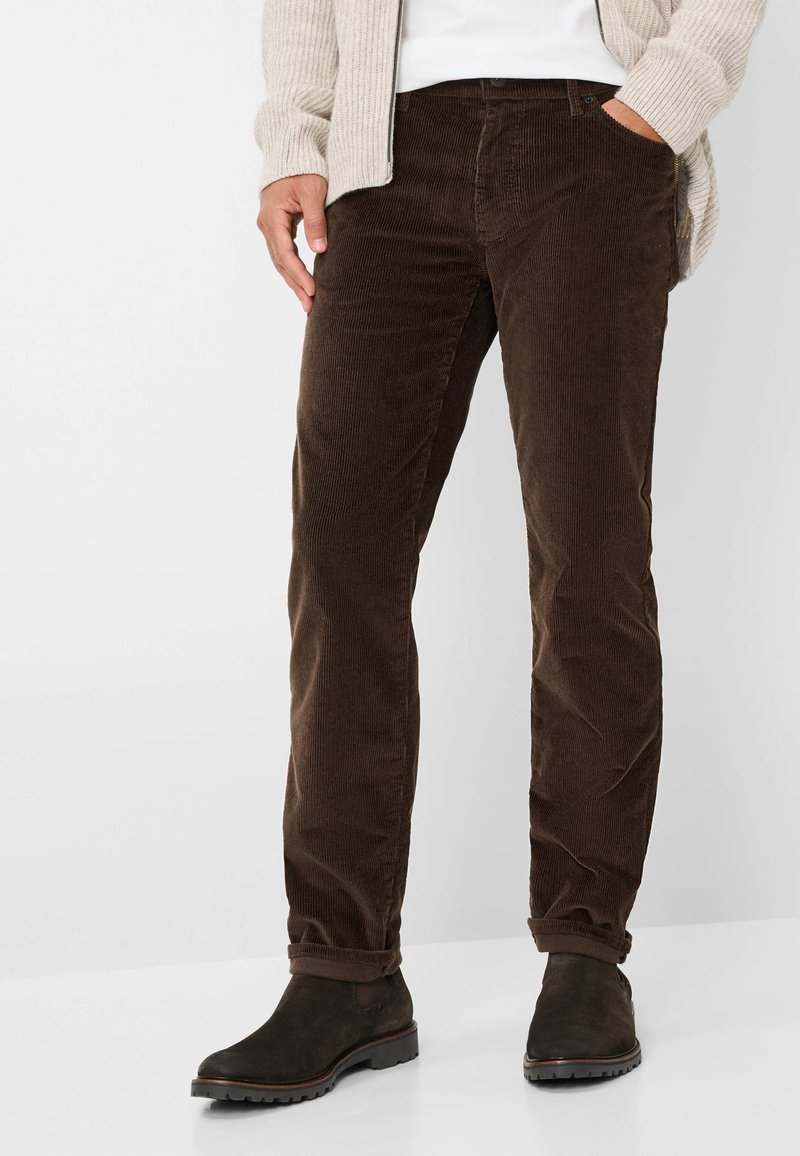 Braune Cordhosen mit strukturierter Oberfläche, slim fit, im fünf-Taschen-Design und hochgekrempelten Säumen, kombiniert mit dunklen Stiefeletten.