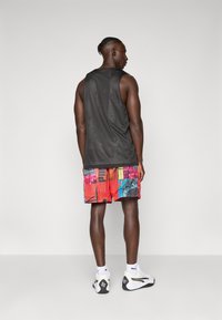 Sort mesh tank top, shorts med multicolor mønster, hvide sneakers med sorte accenter, som viser en slank atletisk silhuet fra ryggen.