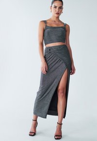 Siva, sjajni dvodijelni outfit s kratkim topom i dugom suknjom s visokim prorezom koja sadrži uvijeni detalj i prstenasti naglasak.