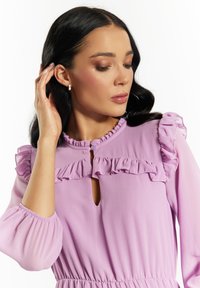 Rochie violet cu accente ondulate la guler și la mâneci, având o deschidere în formă de cheie și o talie ajustată, confecționată dintr-un material ușor.