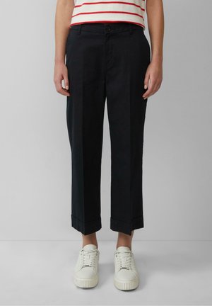 Pantalons coupés en bleu marine foncé avec une coupe décontractée, une fermeture à un bouton et un ourlet retroussé, associés à des baskets blanches.