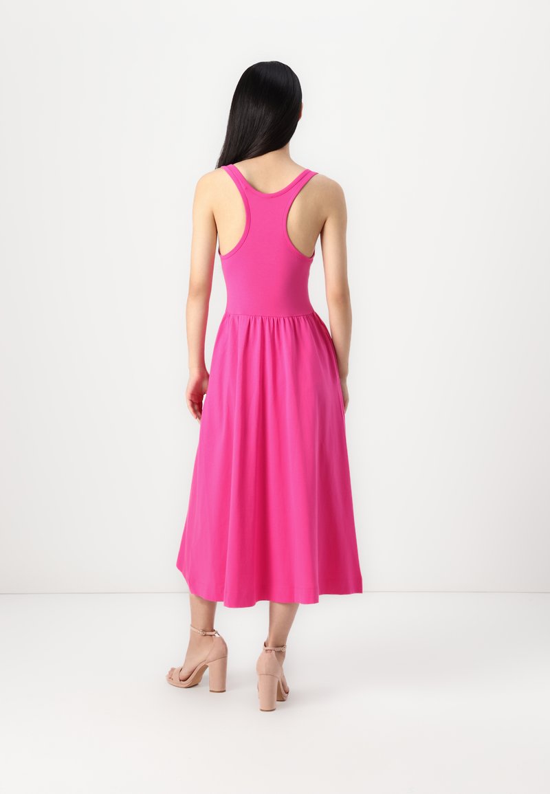Rosa ärmelloses Kleid mit tailliertem Oberteil und ausgestellt Rock. Weicher Stoff mit glatter Textur. Getragen mit hellen Blockabsatzsandalen.