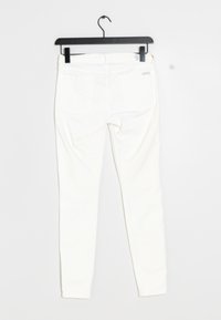 White skinny jeans hanging on black hanger, showing back pockets and stitched seams against white background.