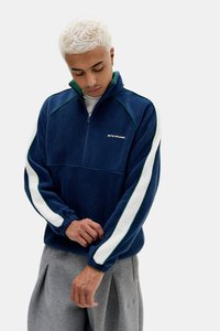 Pullover in felpa navy con accenti verdi e strisce bianche sui lati. Presenta un collo con zip a un quarto e polsini elasticizzati, offrendo una vestibilità comoda.