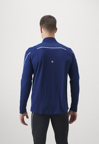 Marineblauwe sportshirt met lange mouwen, witte accentstreepjes, een gladde textuur en een reflecterende cirkelvormige detail op de achterkant.