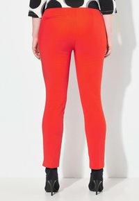 Slim fit červené kalhoty s hladkým povrchem, se skrytou zadní kapsou. V kombinaci s černými vysokými kotníkovými botami.