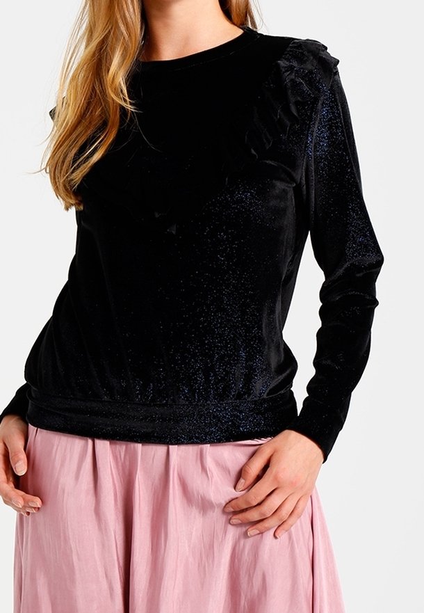 Svart sammetstopp med lång ärm som har en volangkant i halsen, elastisk nederkant och en subtil glans. Kombinationen med en rosa kjol.