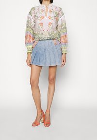 Blouse à motif floral avec manches longues bouffantes et encolure fendue; associée à une jupe plissée en denim et des sandales orange à talons hauts et lanières.