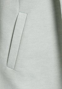 Ljusgrått tyg med texturerad yta, med en sidoficka som smälter in sömlöst i materialet.