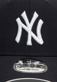 Mustast baseball-müts valge tikitud "NY" logoga. Omab struktureeritud disaini, reguleeritavat rihma ja ümmargust New Era kleebist äärel.