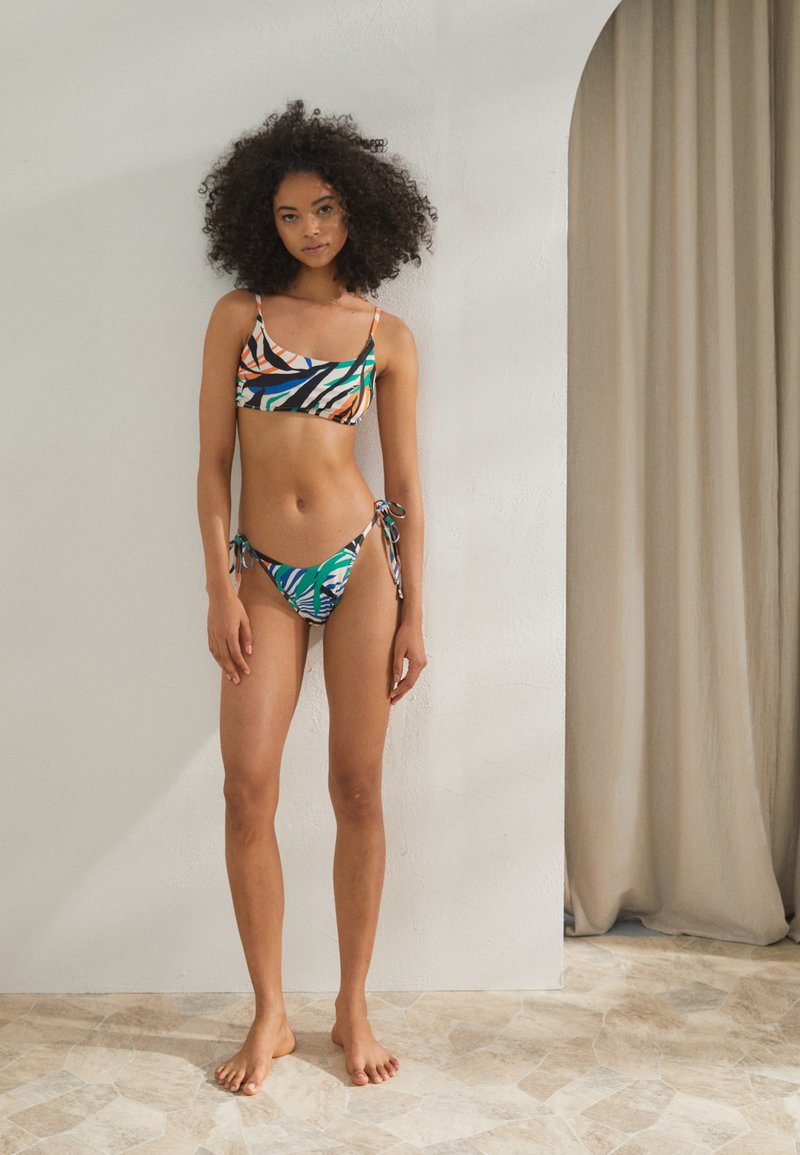 Conjunto de bikini colorido com um top cropped estampado de alças finas e calções laterais com laço combinando, exibindo desenhos vibrantes em verde, laranja e preto.