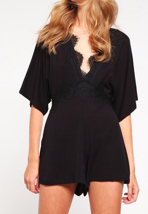 Woman wearing a black lace-trimmed romper with short wide sleeves and a deep V neckline.