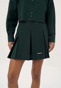 Zwarte geplooide rok van gladde stof, met een aansluitende taille en een logo. Het ontwerp bevat scherpe, gestructureerde plooien en een nette afwerking.