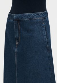 Σκούρα μπλε τζιν φούστα με εμφανείς αντίθετες ραφές και εφαρμοστή ζωνη φορεμένη με μαύρο τοπ.