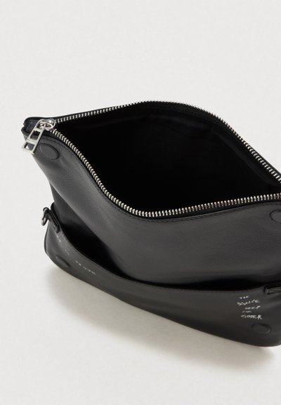 Musta nahkainen pussi, jossa on auki oleva hopeinen vetoketju, pyöreät magneettiset napit sivuilla ja valkoinen teksti "TANSSI PIDÄ LÄHEMPÄ" edessä.