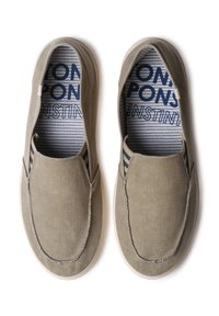 Par beige slip-on fritidssko med hvide såler og stribet inderfor med mørkeblå tekst på hvid baggrund.