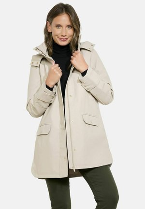 Imperméable beige avec une capuche, des boutons-pression et deux poches avant. Fabriqué en matériau résistant à l'eau, avec une coupe décontractée et des coutures visibles.