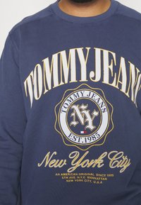Felpa in cotone blu navy con testo audace bianco e giallo: "TOMMY JEANS", "NY" e "New York City", con dettaglio emblema.