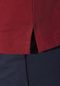 Red cotton shirt with a split hem, paired with dark blue cotton bottoms. The fabric has a smooth texture and a seamless design.