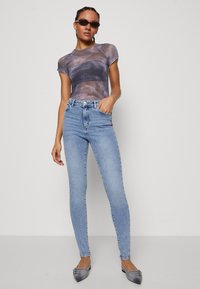 Gjennomsiktig, tie-dye t-skjorte i grå og lilla toner med korte ermer, kombinert med høytlivde, lyseblå, smale jeans og spisse leiligheter.