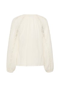 Blouse blanche à manches longues et coupe ample, ornée de panneaux en dentelle sur les manches et les épaules, vue de dos.