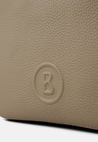 Borsa in pelle beige con superficie texturizzata e logo impresso circolare nell'angolo inferiore.