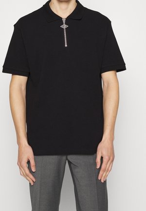 Polo negro de manga corta con cuello de media cremallera. Presenta una textura sutil y una cremallera decorativa con un diseño de ojo.