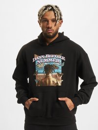 Sort sweatshirt med hætte har et grafisk print af en persons ryg omgivet af sommerfugle og naturskønne landskaber. Frontlomme med kænguru-lukning.
