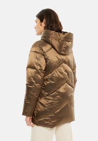 Chaqueta acolchada marrón con capucha, con un acabado brillante y texturizado y costuras diagonales. Diseñada para mantener el calor con una silueta elegante.