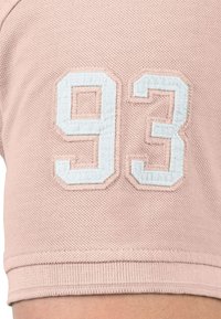 Roze textiel met een gestikt wit nummer "93" op de mouw, voorzien van een hoekig ontwerp en geribbelde zoom.